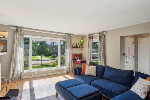 Large windows fill the inviting living room with natural light, highlighting gleaming hardwood floors.