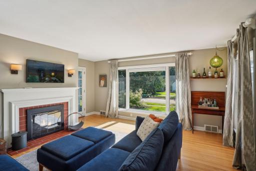 Large windows fill the inviting living room with natural light, highlighting gleaming hardwood floors. Walkout from living room to cozy, sun porch.
