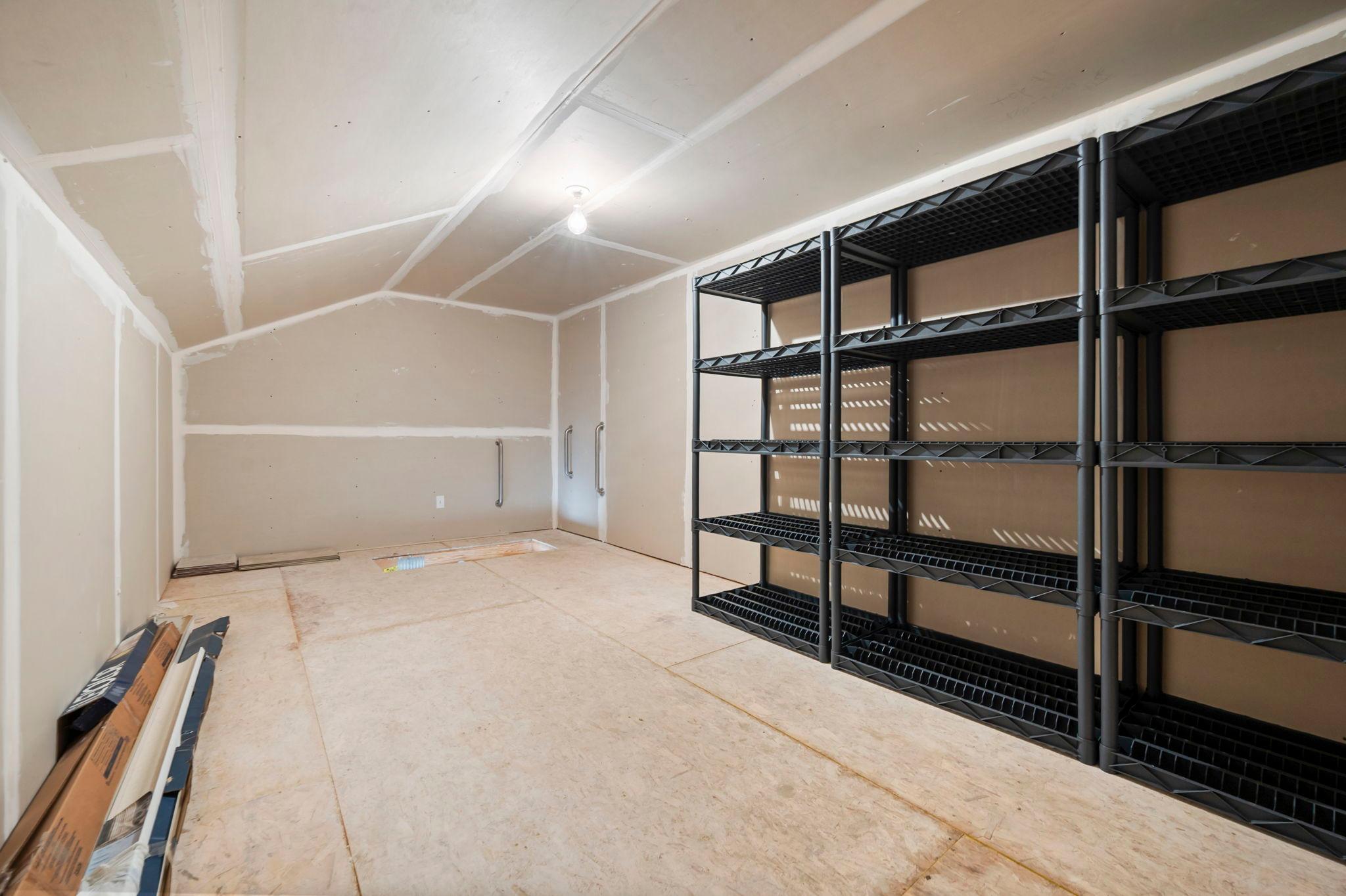 Finished storage area above the garage with pull-down stairs, plenty of storage space, and included shelving. A handrail at the top of the stairs provides added support.