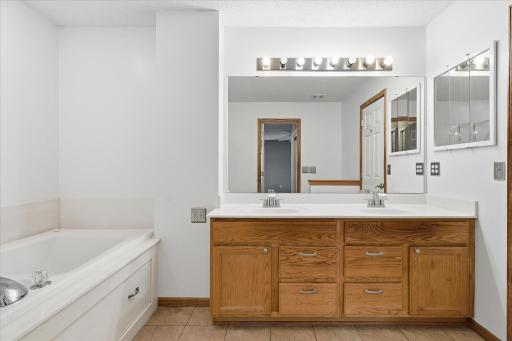 Spacious walk-through full bathroom featuring a large double vanity, updated fixtures, tiled flooring, separate shower, and relaxing soaking tub.