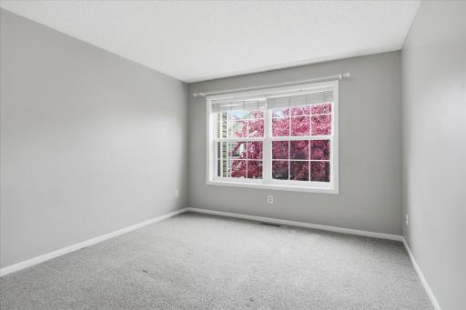 Bright and inviting second bedroom featuring plush newer carpet, neutral finishes, and a large window that fills the space with natural light and beautiful tree views.