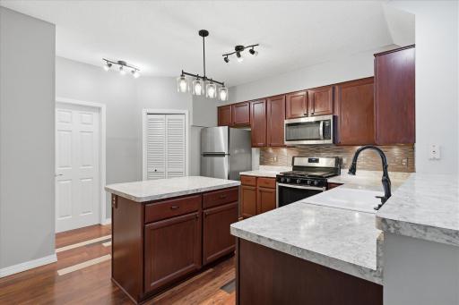Beautifully updated kitchen featuring rich cabinetry, stainless steel appliances, stylish backsplash, breakfast bar seating, and a center island for additional prep space and storage.