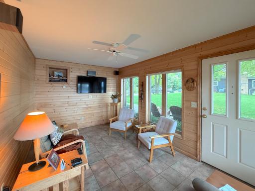 Inviting three-season porch finished with warm wood walls, tile flooring and plenty of windows overlooking the lakeside yard.