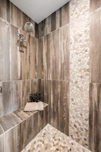 Oversized walk-in shower combines beautiful finishes with exceptional functionality. Faux-wood plank tile surrounding the shower adds warmth and texture.