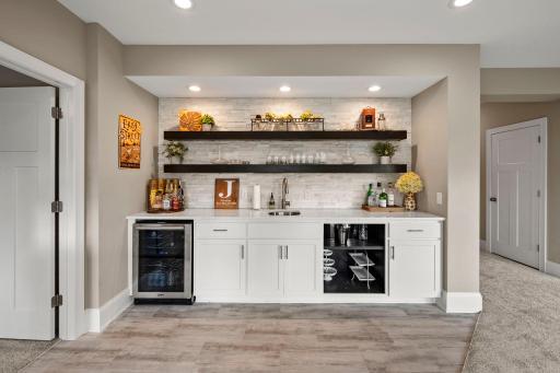 White lower cabinetry and quartz countertops create a clean, polished look. Built-in sink and beverage refrigerator add convenience for hosting. Open wood shelving provides stylish display and storage space above the bar.