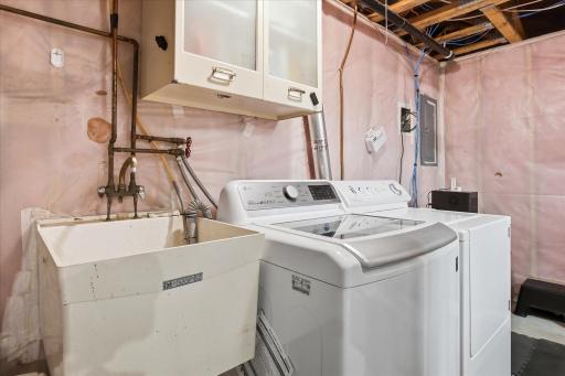 Dedicated laundry area with full-size washer and dryer, utility sink, and additional cabinet for practical household organization.