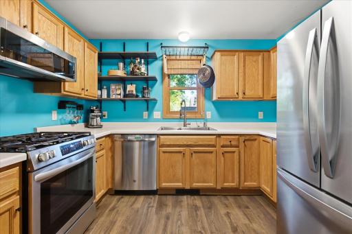 Bright and functional kitchen featuring abundant cabinetry, stainless steel appliances, generous counter space, open shelving, and a large window over the sink.