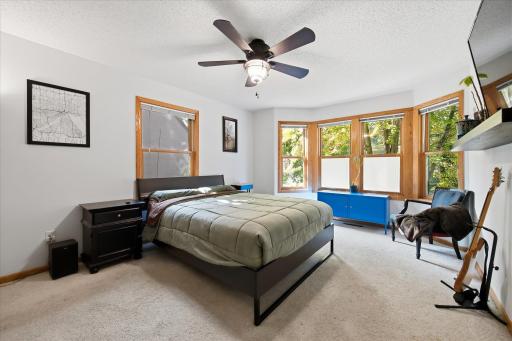The primary bedroom features plush carpeting, ceiling fan, and a charming bay of windows overlooking the tree-lined surroundings.