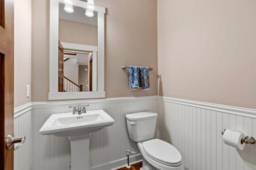 A charming main-level powder bath features classic wainscoting and a pedestal sink.