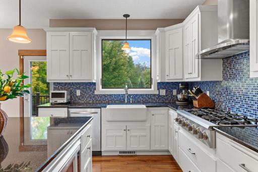 A farmhouse-style sink sits beneath a large window overlooking the backyard, surrounded by granite countertops and extensive cabinetry.