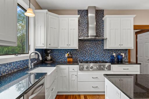 A professional 6-burner range is framed by a statement range hood and striking tile backsplash, creating a beautiful focal point in the kitchen.