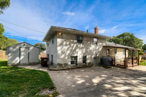 Rear exterior view showcasing the covered deck, expansive driveway, yard, and one of two large storage sheds