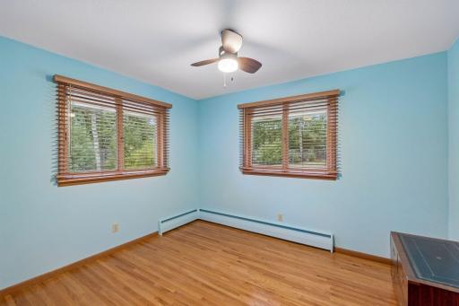Two double windows fill the second main floor bedroom with natural light, complemented by hardwood flooring, a ceiling fan with light, and a closet.
