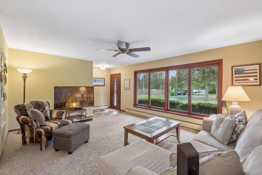 Huge windows bring natural light into the spacious living room, complemented by carpet flooring, a ceiling fan, and ample room for relaxing or entertaining