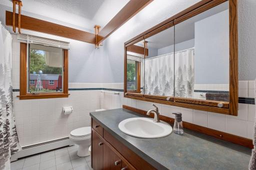 A bright window brings natural light to the main floor full bath, complete with tile flooring, a vanity, mirrored storage, and a tub/shower combination. Plus cool FLW style custom lighting