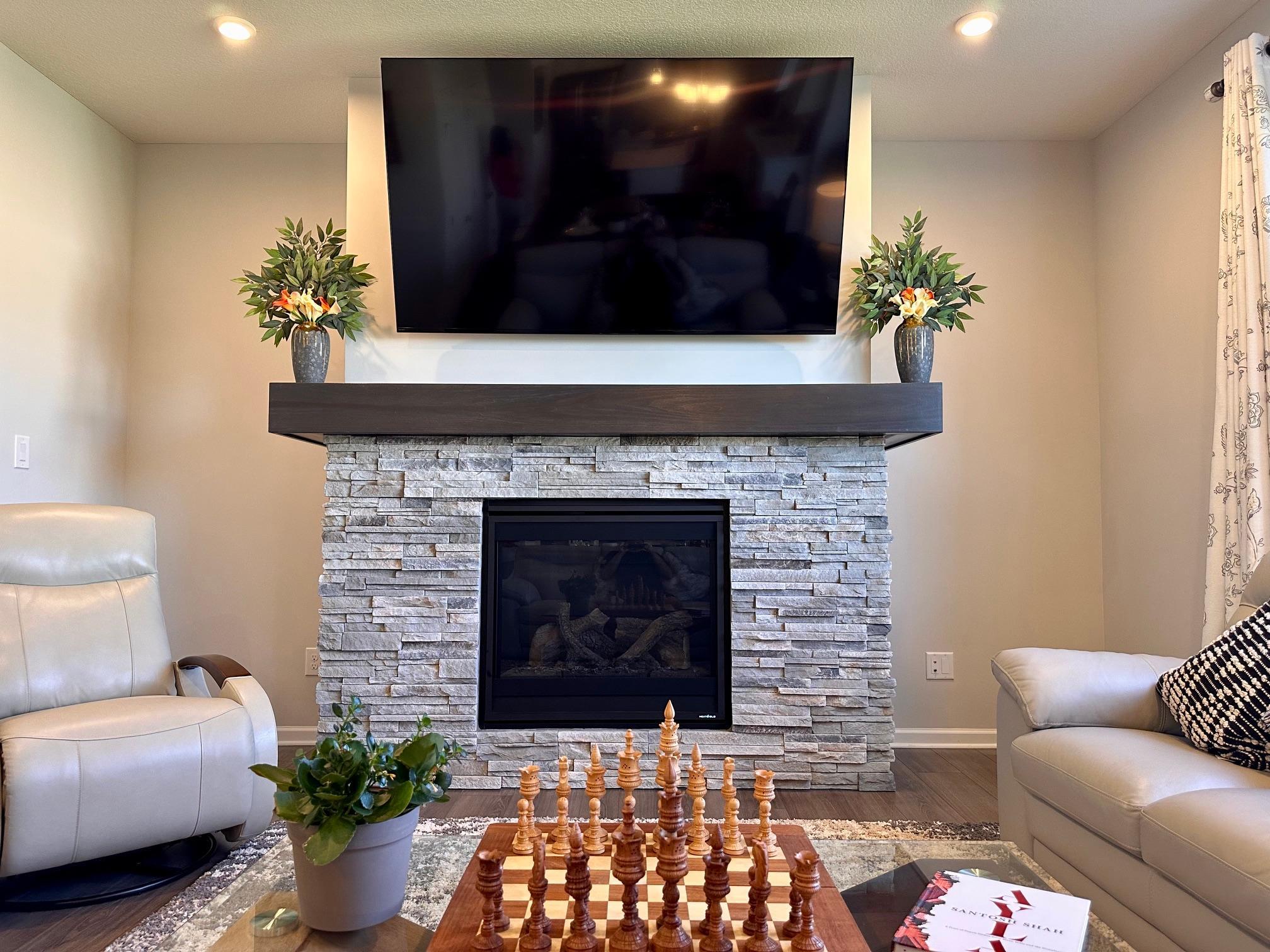 Beautiful stack-stone, glass fireplace with a mantel serves as a focal point in the family/living room.jpeg