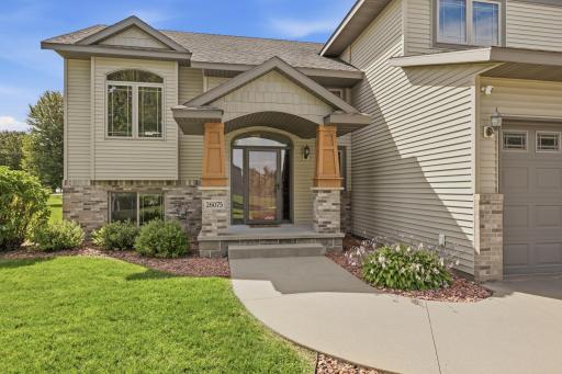 Vinyl siding with a brick-accented front, dual pillars, an arched covered entry, decorative block accents, and an Andersen full-glass storm door.
