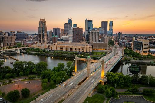 A breathtaking panorama captures the Mississippi River, glowing bridges, and Downtown Minneapolis at sunset.