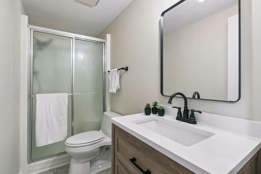 The lower-level 3/4 bathroom has been refreshed with a new vanity, flooring, lighting and mirror. The crisp white countertop and contrasting black fixtures add a modern touch, while the walk-in shower completes this functional space.