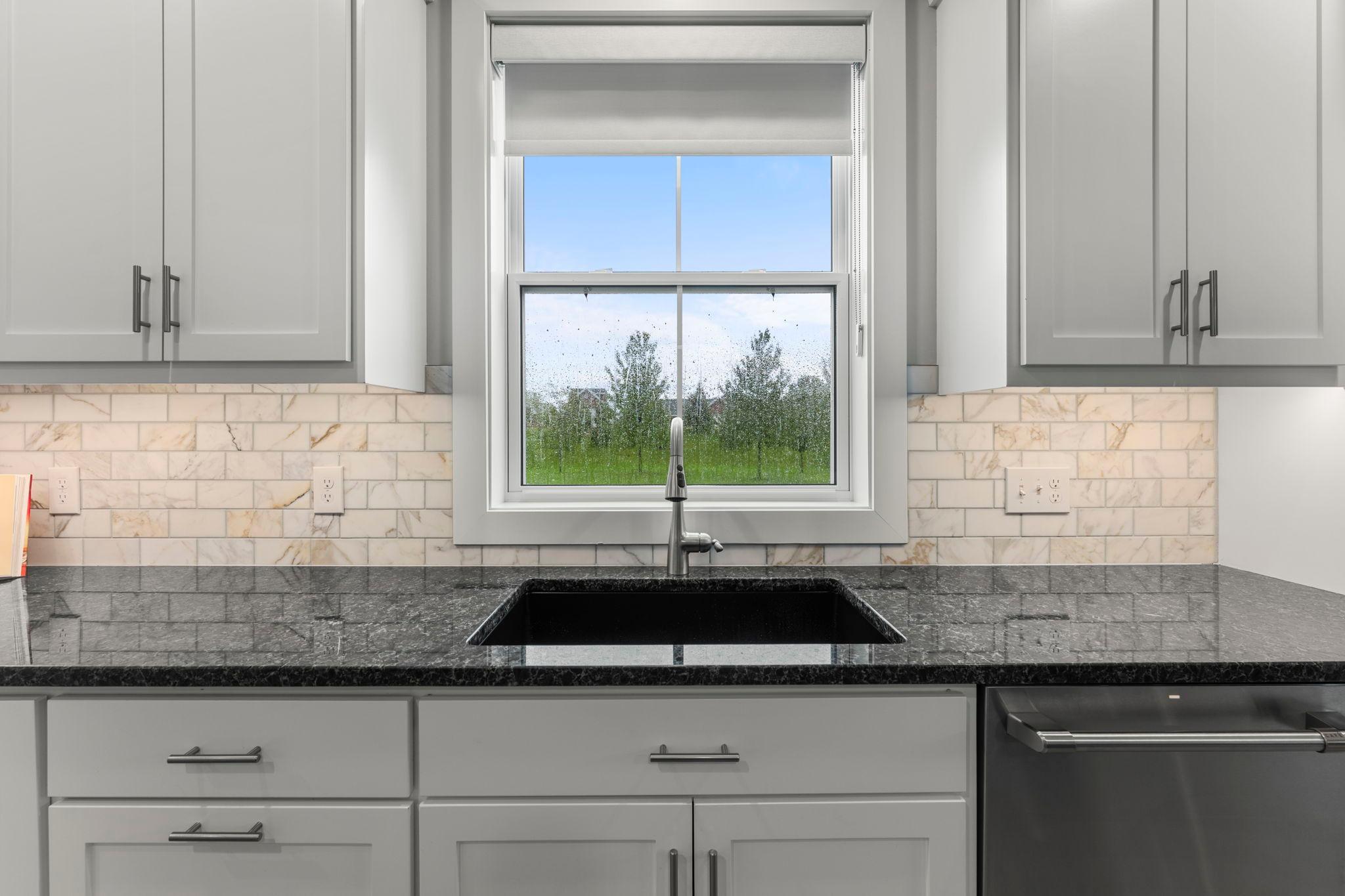 The kitchen features a large window offering a clear view of the spacious, flat backyard. The berm at the rear of the yard ensures privacy.