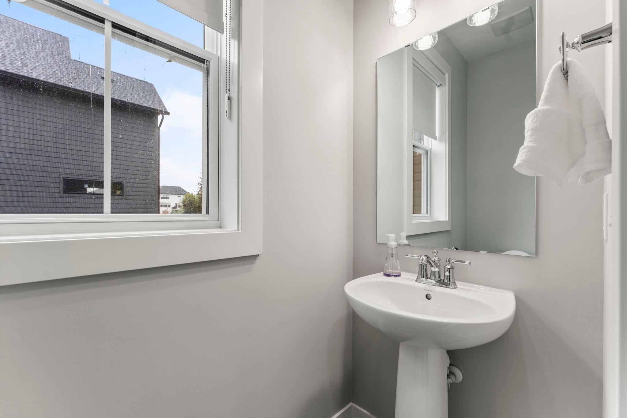 The main level includes a convenient 1/2 bathroom featuring ceramic tile floors, a pedestal sink, and a large window that fills the room with natural light.