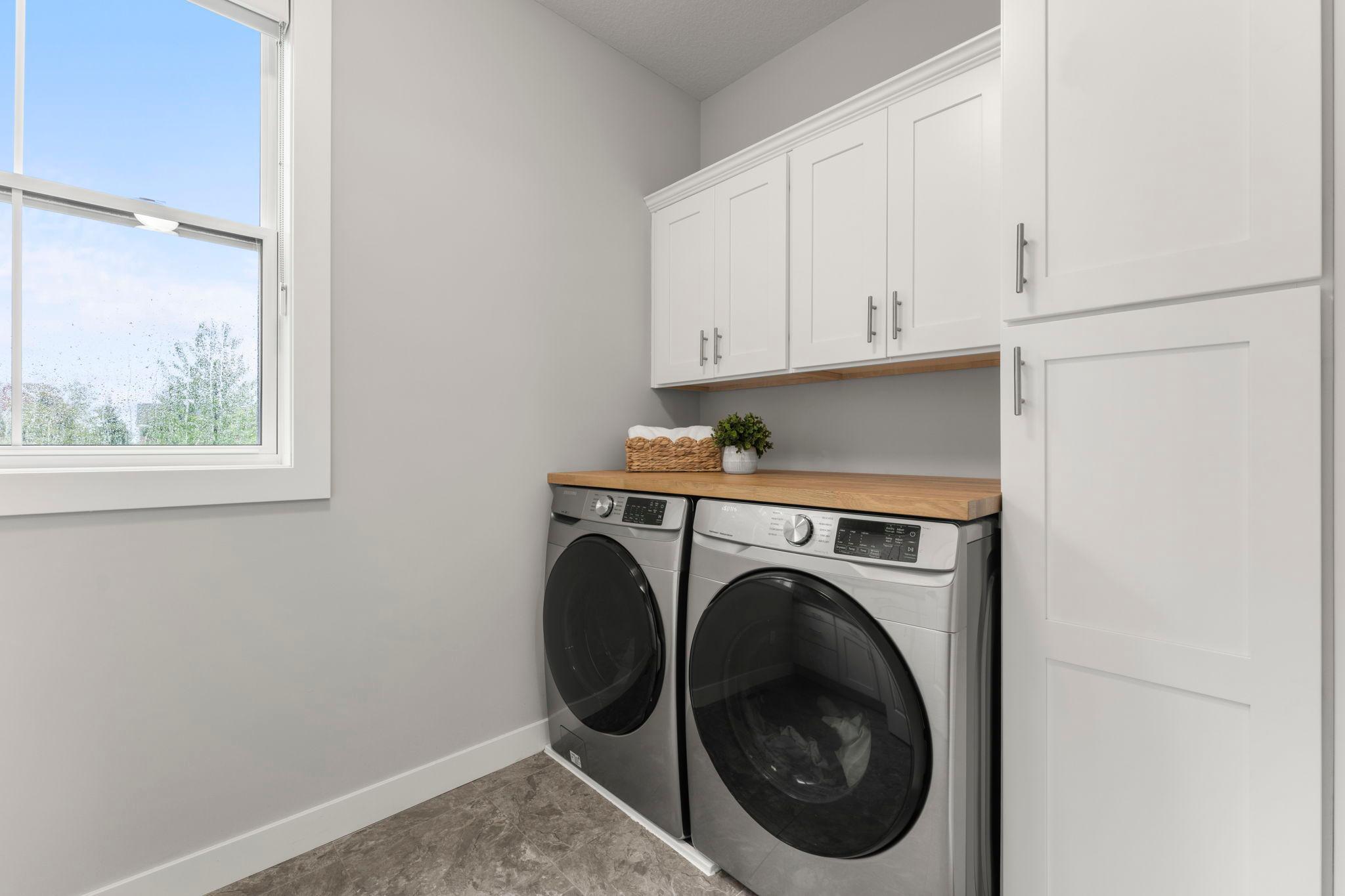 The main-level laundry room off the mudroom features a stainless-steel Samsung front-load washer and dryer, ceramic-tile floors, and a large window that fills the room with natural light.