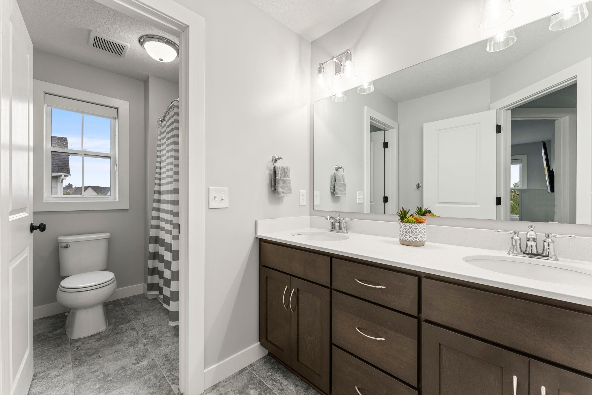 The upper level also has a full bathroom with a ceramic-tile floor, a comfort-height dual-sink vanity with storage, and a separate water closet with a tub and a window.
