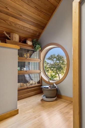 Bright upper-level landing features a unique round window, built-in wood display shelving and hardwood floors.