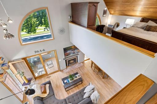 Elevated view showcases the home's open, airy design with soaring ceilings, extensive wood paneling, arched windows, hardwood floors, fireplace, and seamless connection between the living and upper-level spaces.