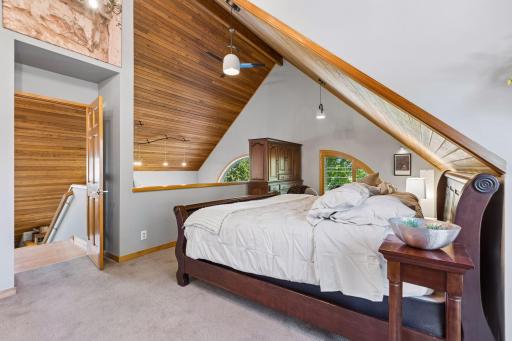 Another view of the spacious primary suite highlights the vaulted wood ceiling, distinctive architectural details, generous closet storage, and open connection to the upper-level landing.