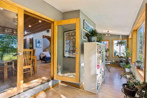 A bright, sun-filled transition space leads toward the three-season porch, offering another peaceful spot to enjoy views of the beautifully landscaped grounds.