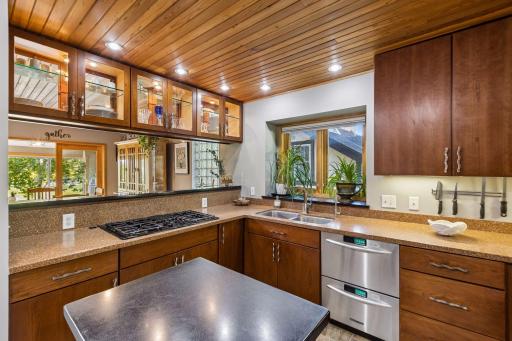 Well-appointed kitchen with custom wood cabinetry, glass-front uppers, generous counter space, gas cooktop, stainless steel appliances, and a convenient center island.