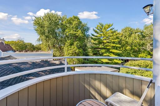 Private upper-level balcony provides a peaceful outdoor retreat surrounded by mature trees, with space for seating and views overlooking the surrounding neighborhood.