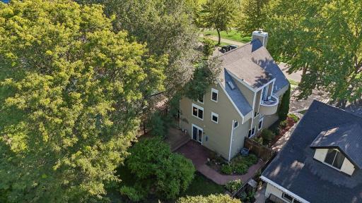 Aerial view showcasing the home's private, tree-lined setting, landscaped yard, rear patio and deck areas, and surrounding neighborhood.