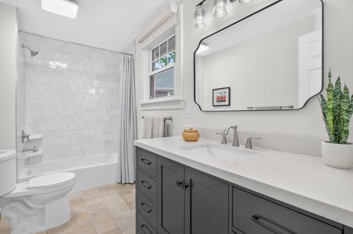 The beautifully renovated secondary bath pairs heated tile floors with a thoughtfully tiled tub surround and elegant quartz-topped vanity.