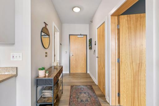 This welcoming condo entry features warm wood flooring, natural wood doors, neutral finishes, and a thoughtfully styled hallway.