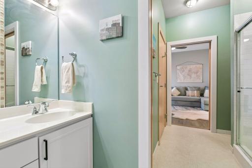 Fresh, inviting en-suite bathroom with a white vanity, large mirror, glass-enclosed shower, and calming green walls.
