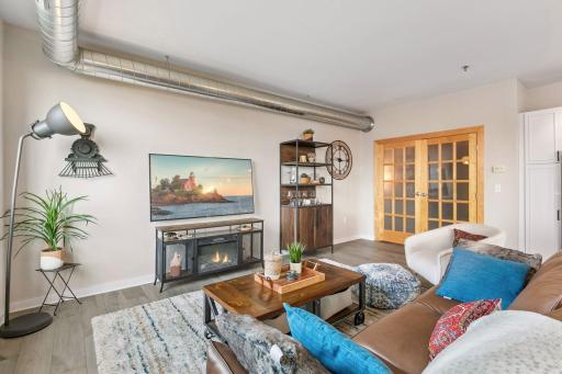 The spacious and inviting living room features an open-concept layout, contemporary lighting, exposed ductwork, and warm wood-look flooring.