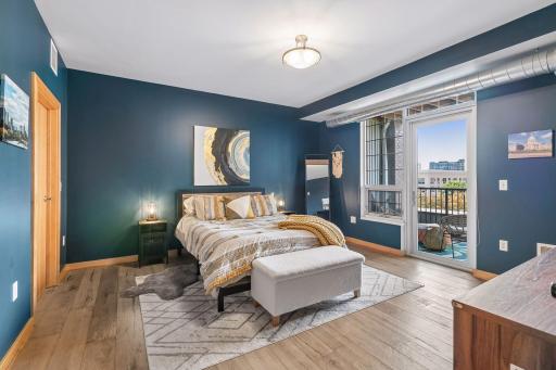 Spacious primary bedroom featuring rich blue walls, large windows, comfortable sitting area, and direct access to the private balcony.