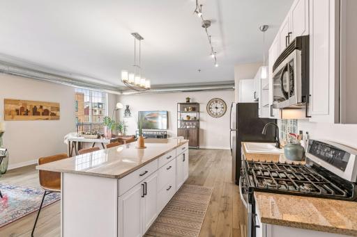 White cabinetry, a large center island, stainless steel appliances provide a clean, functional setting, while exposed ductwork and contemporary lighting add an urban loft-inspired character.
