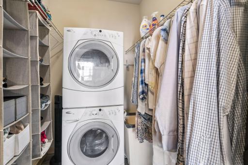 Convenient laundry room with stacked washer and dryer, extensive shelving, hanging space, and excellent organizational storage.