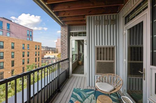 Spacious covered balcony with composite decking, decorative railing, string lighting, and seating area overlooking the surrounding cityscape.