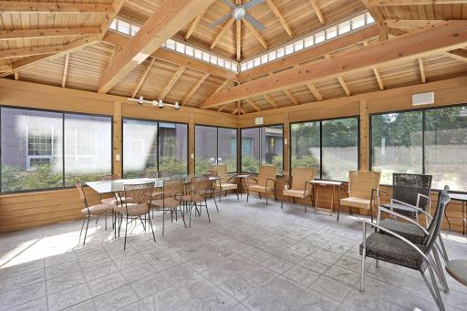 Bright interior of the community gazebo featuring a vaulted wood-beamed ceiling, ceiling fan, expansive screened windows, and ample seating for residents and guests.
