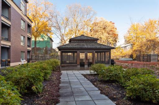The peaceful courtyard walkway leads to a spacious screened gazebo, surrounded by mature landscaping and greenery.
