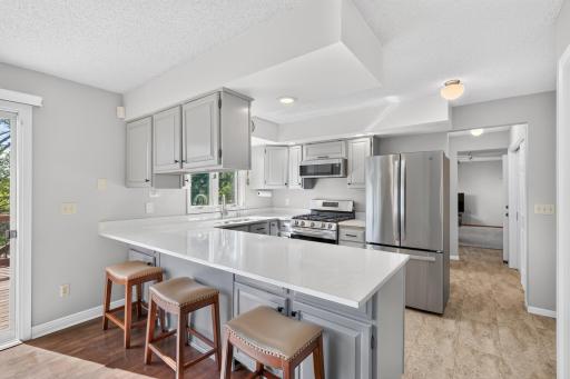 Updated kitchen (2022) features painted cabinetry, expansive quartz countertops, stainless steel appliances and a breakfast bar with seating.