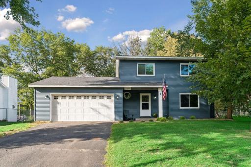 Blue vinyl siding, white trim, and mature trees frame the front exterior.
