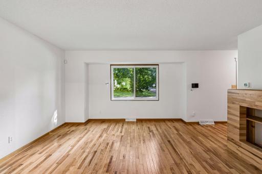 Large living room window overlooks the front yard and mature trees.