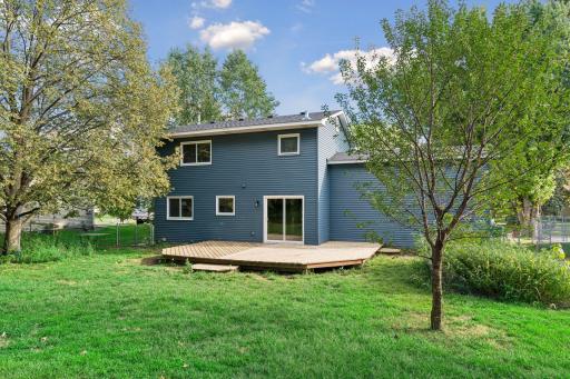 Backyard view of the home, deck, and surrounding greenery.