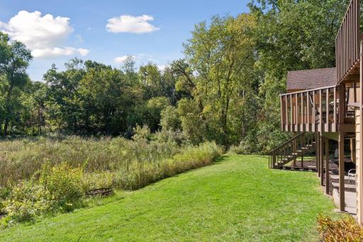 Spacious backyard with mature trees, pond views, and multiple outdoor living spaces surrounded by nature.