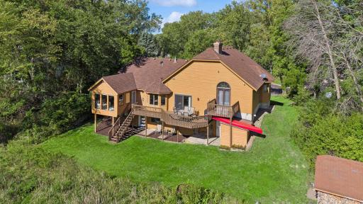 Rear aerial view showcases the spacious backyard, multiple decks, 3-season porch, walkout lower level, mature trees, and private pond setting.